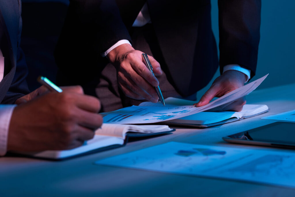Duas mãos de empresários analisando documentos e gráficos em papel, representando a análise de dados judiciais para prevenção da litigância predatória.