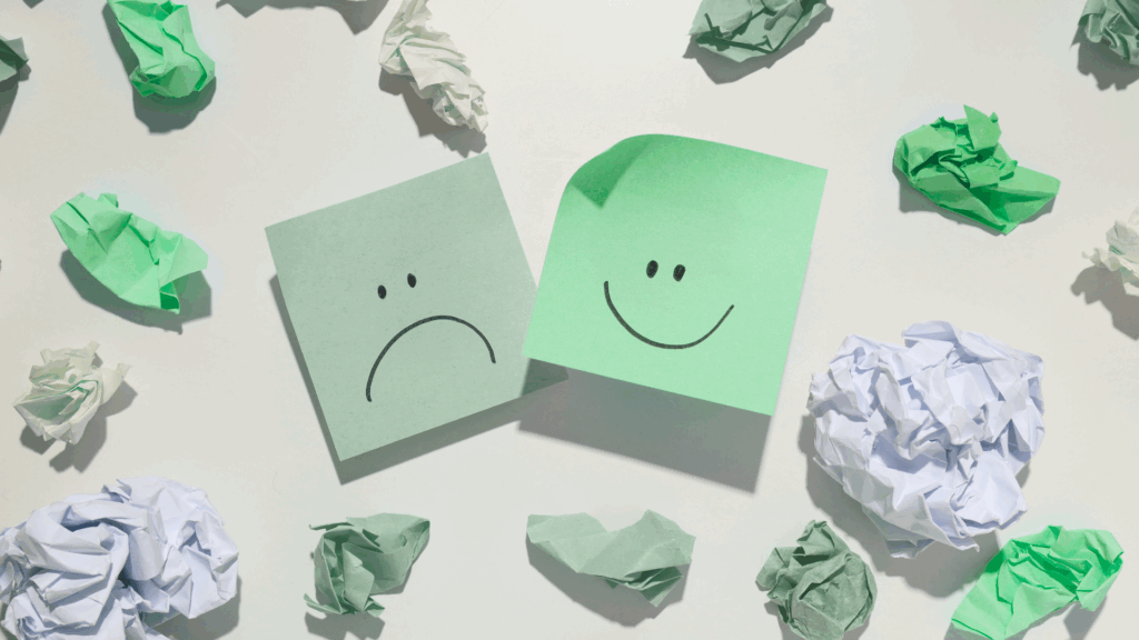 Painel coberto de post-its com rostos desenhados, um feliz e outro triste, simbolizando os desafios emocionais no ambiente de trabalho e os efeitos do burnout nas empresas em 2025.